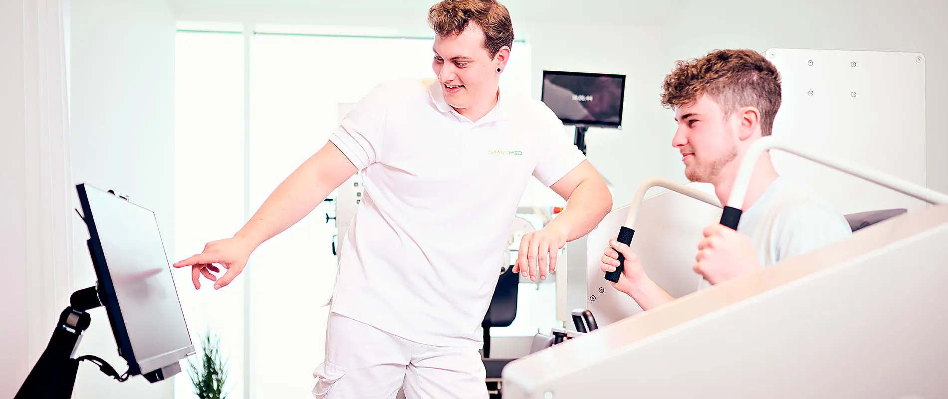 Ein Therapeut von SaanoMed zeigt einem jungen Patienten am POWERSPINE-Gerät die Messwerte auf dem Monitor